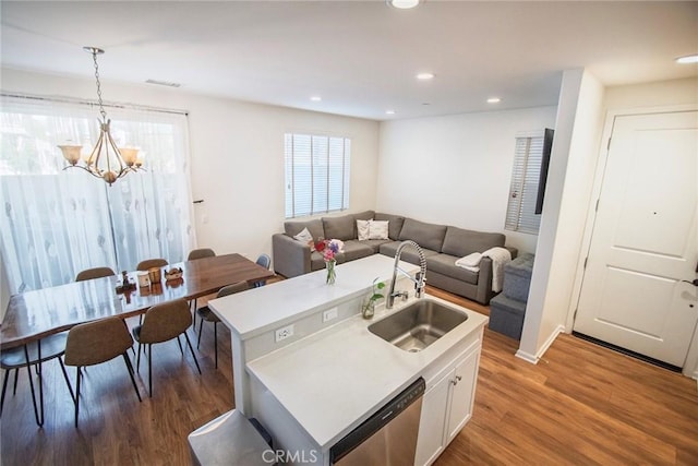 kitchen with white cabinets, a notable chandelier, a sink, wood finished floors, and stainless steel dishwasher