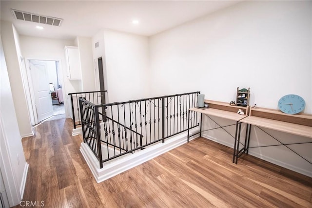 corridor with visible vents, wood finished floors, baseboards, an upstairs landing, and recessed lighting