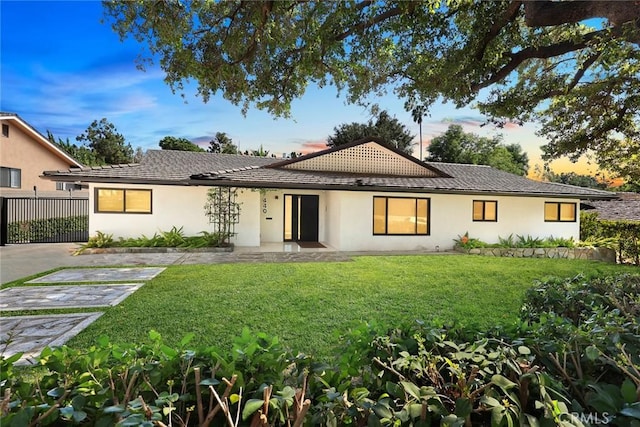 rear view of house featuring a lawn, fence, stucco siding, and a tile roof