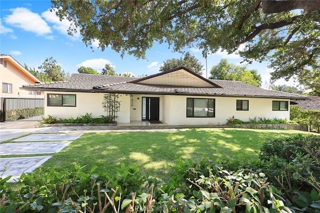 ranch-style home featuring fence, a tile roof, a front yard, and stucco siding