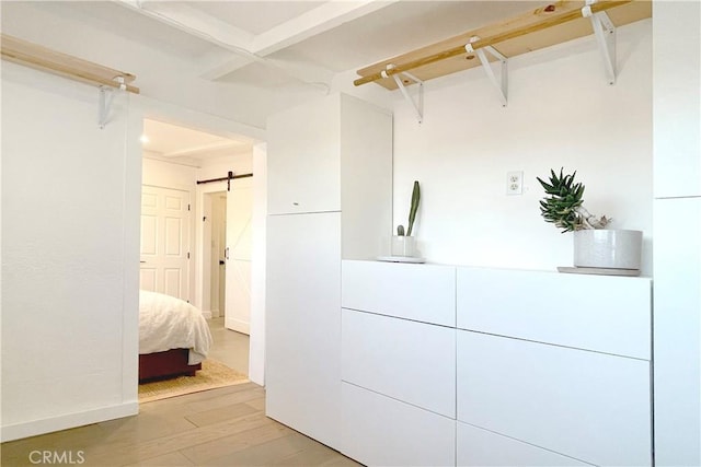 walk in closet with beamed ceiling, a barn door, and light wood finished floors