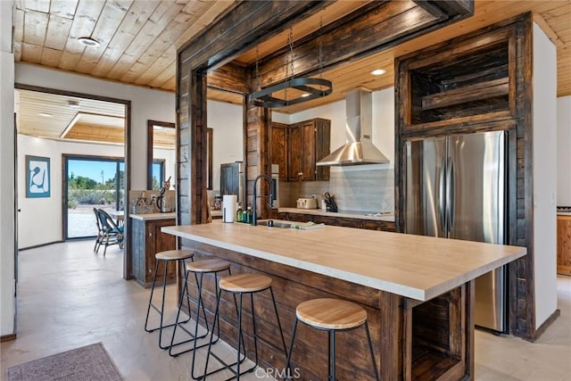 kitchen with wall chimney range hood, decorative backsplash, wooden ceiling, freestanding refrigerator, and concrete floors