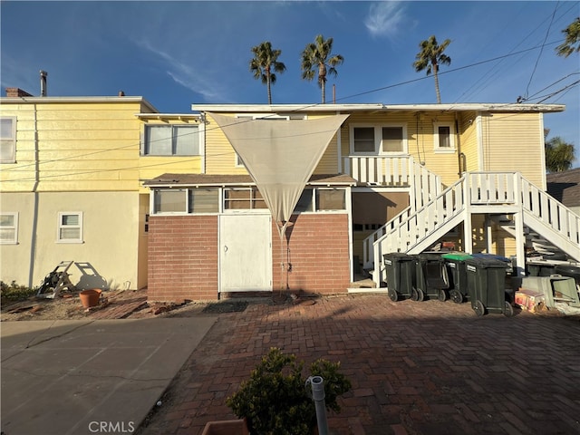 rear view of house featuring stairs and brick siding