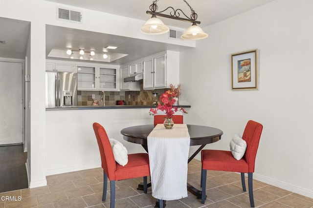 dining space with a tray ceiling, visible vents, and baseboards
