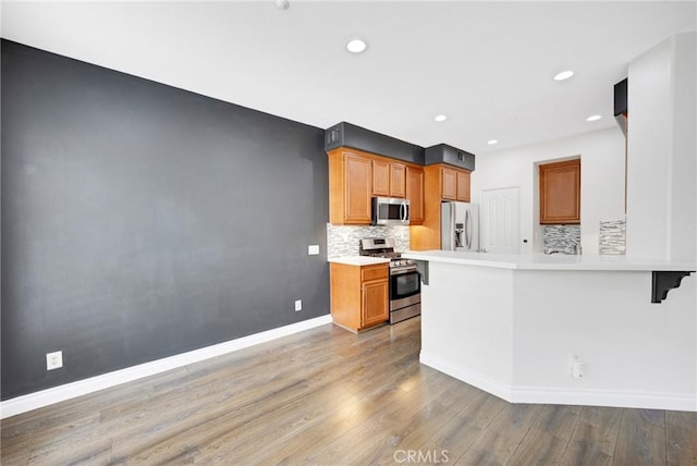 kitchen with decorative backsplash, a peninsula, baseboards, light wood finished floors, and stainless steel appliances