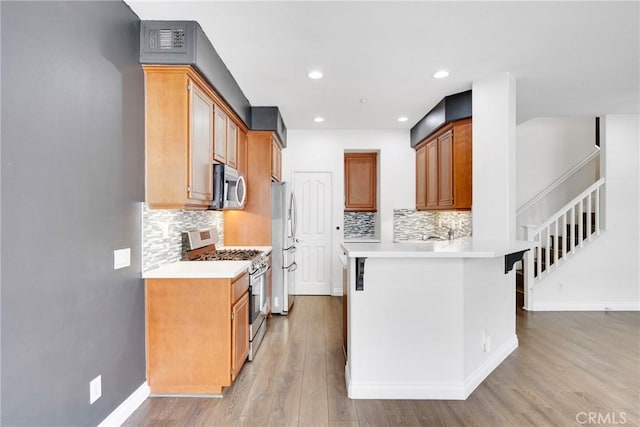 kitchen featuring decorative backsplash, baseboards, light wood-type flooring, light countertops, and appliances with stainless steel finishes