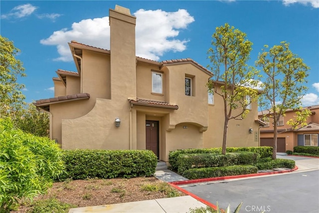 mediterranean / spanish house featuring a chimney, a garage, stucco siding, and a tile roof