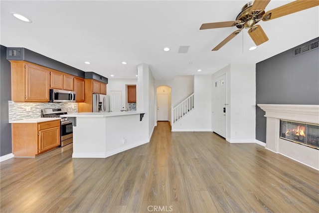 kitchen with light countertops, stainless steel appliances, decorative backsplash, light wood-type flooring, and visible vents