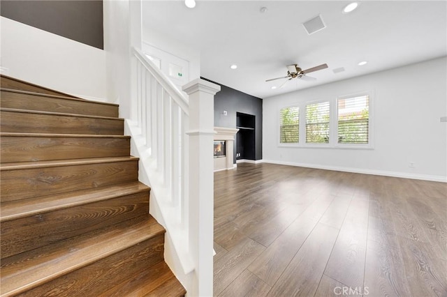 stairway featuring ceiling fan, a glass covered fireplace, recessed lighting, baseboards, and wood finished floors
