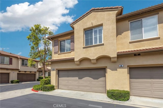 multi unit property with an attached garage, a tile roof, and stucco siding