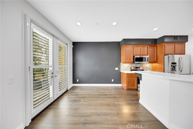 kitchen featuring appliances with stainless steel finishes, light countertops, recessed lighting, decorative backsplash, and wood finished floors
