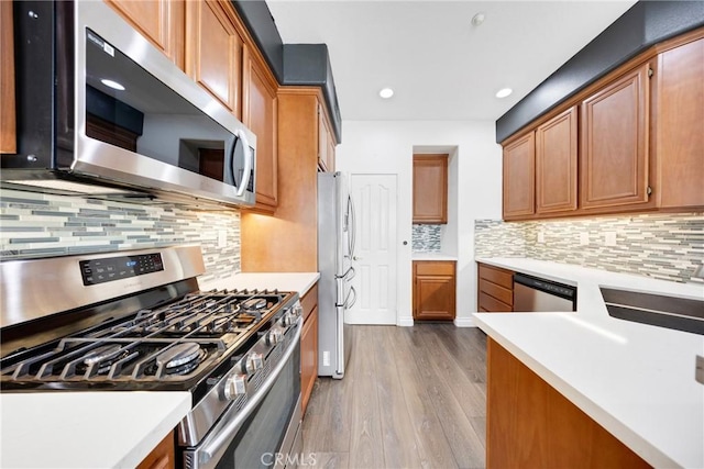 kitchen with decorative backsplash, appliances with stainless steel finishes, brown cabinets, wood finished floors, and light countertops