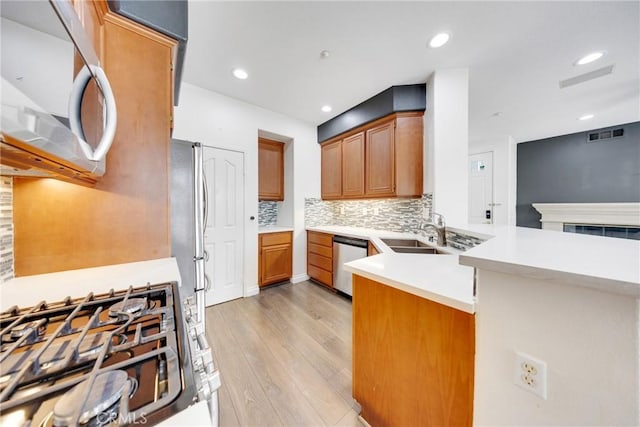 kitchen featuring brown cabinets, a sink, light wood-style flooring, appliances with stainless steel finishes, and backsplash