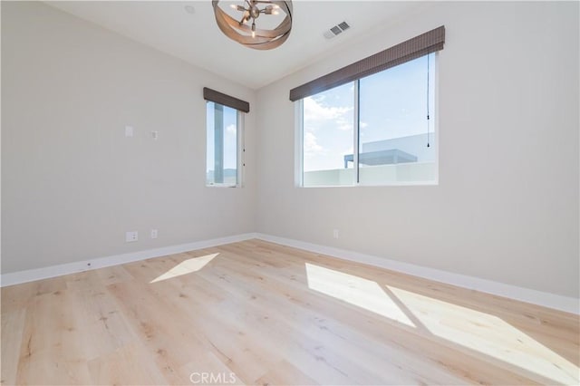 empty room with visible vents, baseboards, wood finished floors, and a notable chandelier