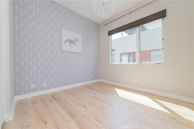 spare room with baseboards, wood finished floors, a chandelier, and wallpapered walls