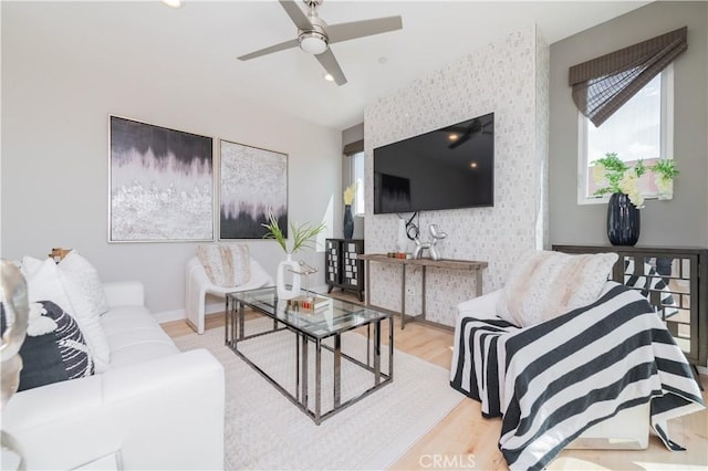 living room with a ceiling fan, an accent wall, wood finished floors, and wallpapered walls
