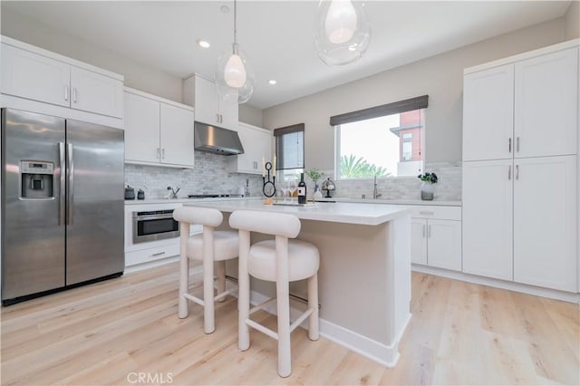 kitchen featuring stainless steel fridge, white cabinetry, under cabinet range hood, tasteful backsplash, and light wood-style flooring