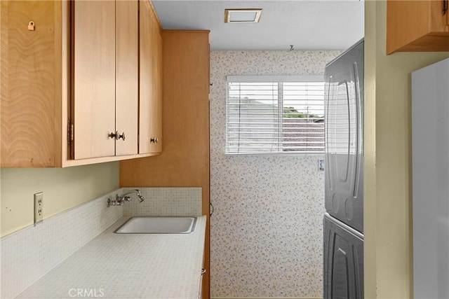 laundry area featuring stacked washer / dryer, wallpapered walls, and a sink