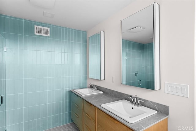 bathroom featuring double vanity, visible vents, a shower stall, and a sink
