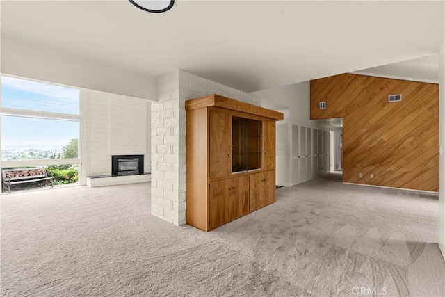 interior space with wooden walls, carpet flooring, a brick fireplace, and visible vents