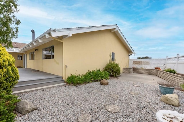 rear view of house with stucco siding, a patio area, fence, and a wooden deck
