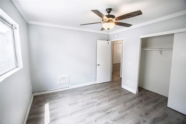 unfurnished bedroom with a closet, ornamental molding, wood finished floors, baseboards, and a ceiling fan