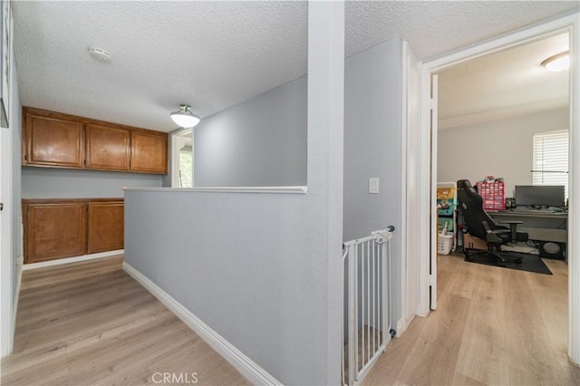 corridor featuring a textured ceiling, an upstairs landing, plenty of natural light, and light wood-style flooring