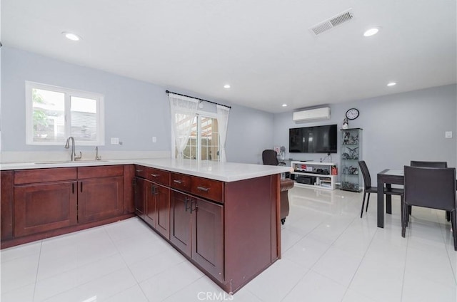 kitchen with visible vents, a wall mounted air conditioner, dark brown cabinets, a sink, and light countertops