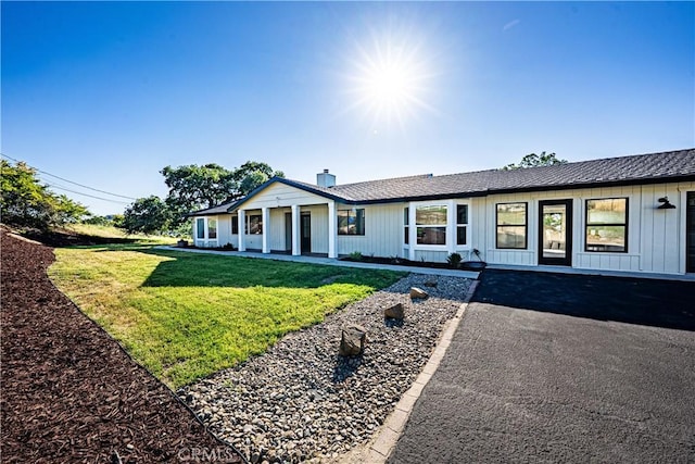 view of front of home with a front yard, a chimney, covered porch, and board and batten siding