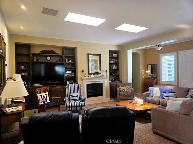 living area with visible vents, built in features, arched walkways, a fireplace with flush hearth, and a skylight