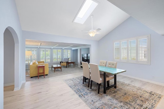dining area featuring ceiling fan, arched walkways, wood finished floors, baseboards, and lofted ceiling with skylight