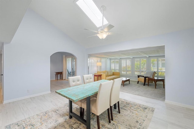 dining area with baseboards, lofted ceiling with skylight, ceiling fan, arched walkways, and light wood finished floors