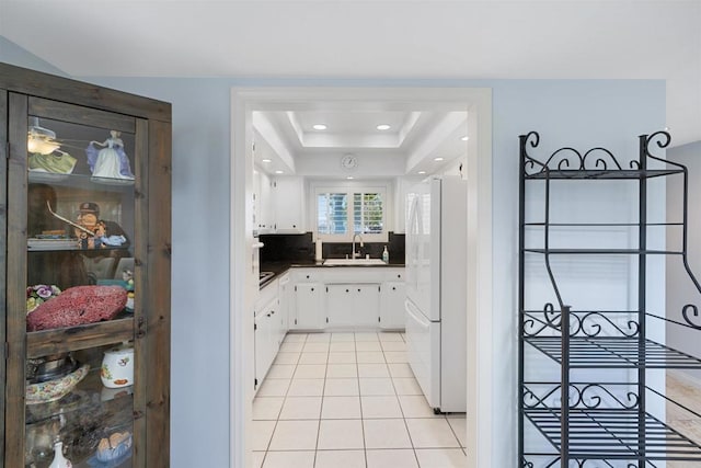 kitchen with white cabinets, light tile patterned flooring, dark countertops, a sink, and freestanding refrigerator