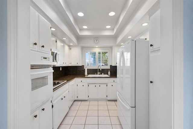 kitchen featuring dark countertops, a sink, white appliances, light tile patterned floors, and backsplash