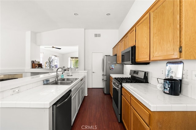 kitchen with appliances with stainless steel finishes, a sink, dark wood finished floors, lofted ceiling, and visible vents