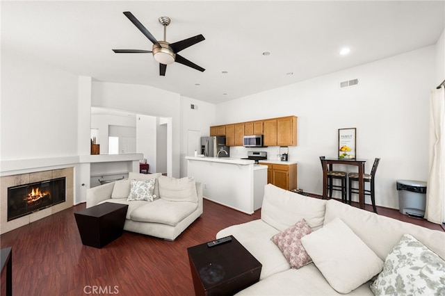 living area featuring ceiling fan, dark wood finished floors, a tiled fireplace, vaulted ceiling, and visible vents