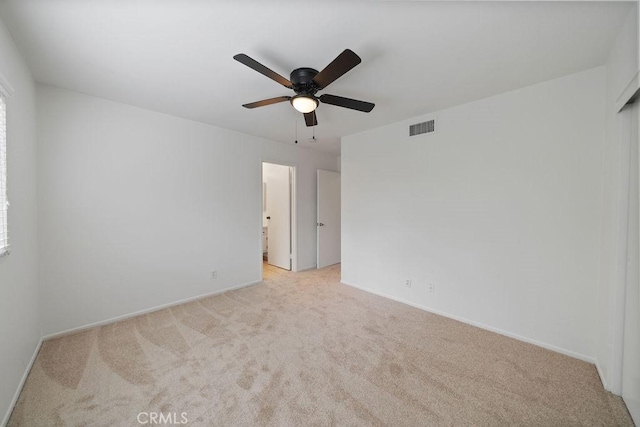 empty room with baseboards, visible vents, ceiling fan, and light colored carpet