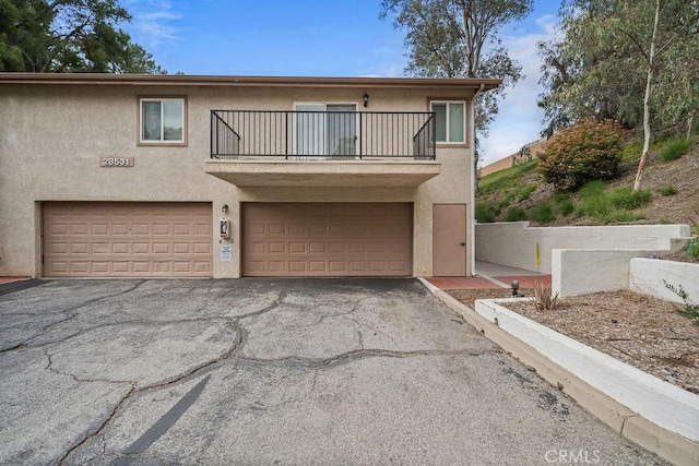 view of front of house with an attached garage, aphalt driveway, a balcony, and stucco siding