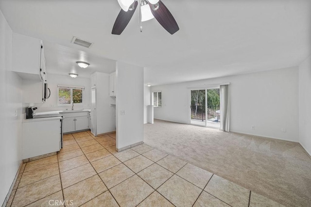 unfurnished living room with a ceiling fan, light colored carpet, light tile patterned flooring, and a wealth of natural light