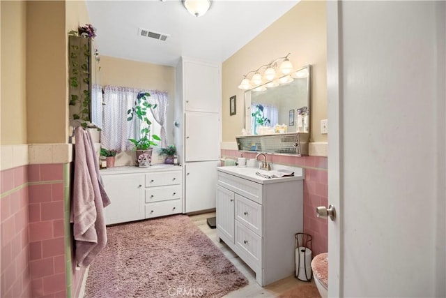 full bathroom with tile walls, a wainscoted wall, vanity, and visible vents
