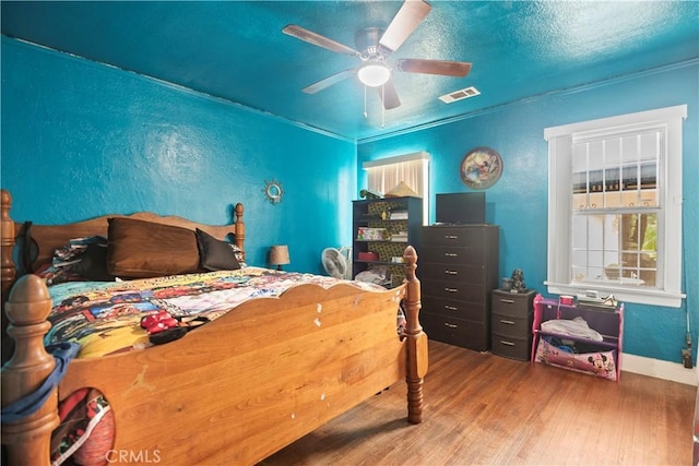 bedroom featuring ceiling fan, a textured ceiling, baseboards, wood finished floors, and visible vents