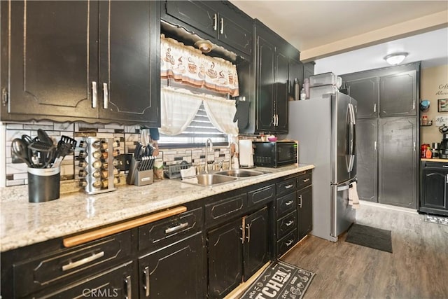 kitchen featuring decorative backsplash, freestanding refrigerator, wood finished floors, black microwave, and a sink