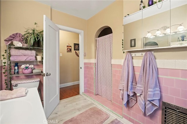 full bath featuring tile walls, a wainscoted wall, and wood finished floors