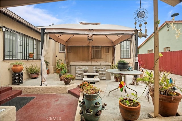 view of patio featuring a hot tub, a gazebo, and fence