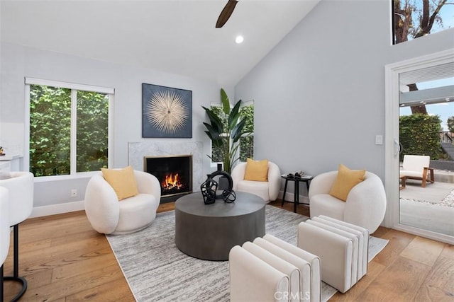 living area with high vaulted ceiling, a premium fireplace, ceiling fan, plenty of natural light, and light wood-style floors