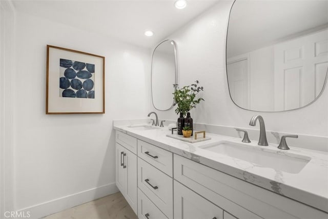 bathroom with baseboards, double vanity, marble look tile flooring, and recessed lighting