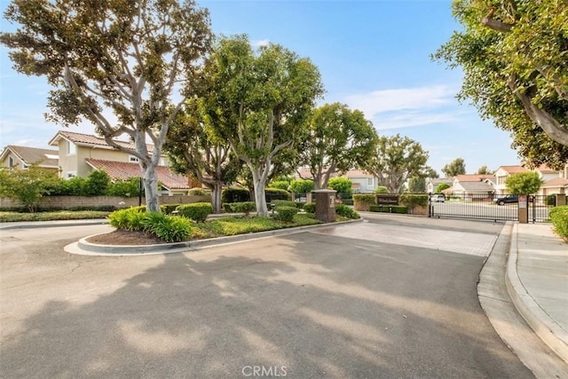 view of asphalt road with a gate, a residential view, curbs, and a gated entry