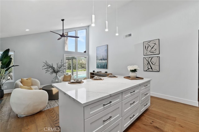 kitchen with a towering ceiling, ceiling fan, light wood-type flooring, white cabinetry, and baseboards