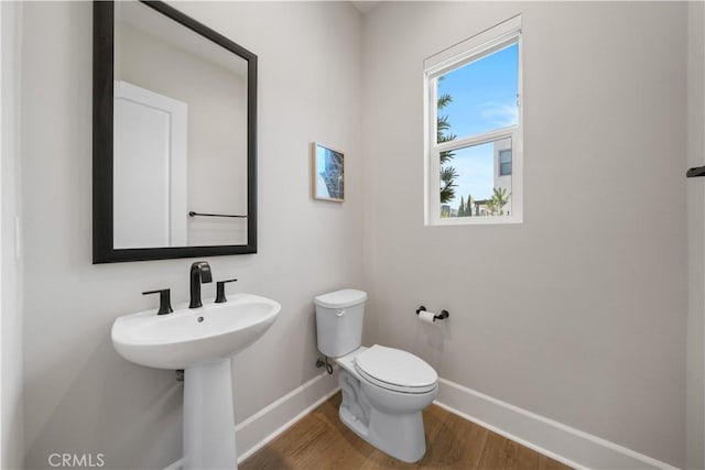half bath featuring toilet, baseboards, a sink, and wood finished floors