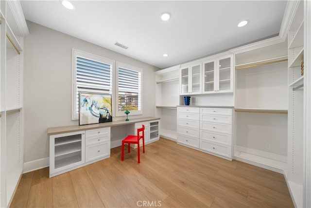walk in closet featuring visible vents, built in desk, and light wood finished floors